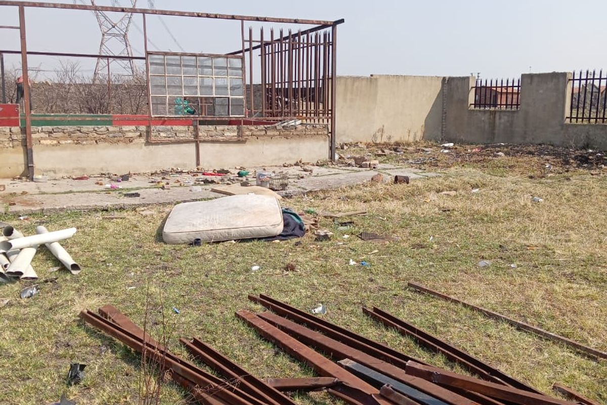An industrial outdoor area featuring a concrete slab, steel structural framing, and perimeter security walls, currently requiring significant site clearance and maintenance.