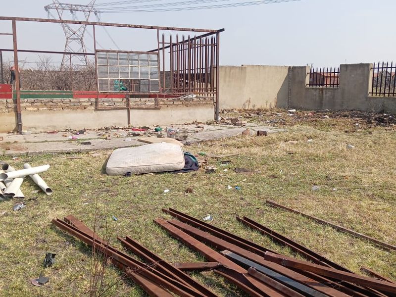 An industrial outdoor area featuring a concrete slab, steel structural framing, and perimeter security walls, currently requiring significant site clearance and maintenance.