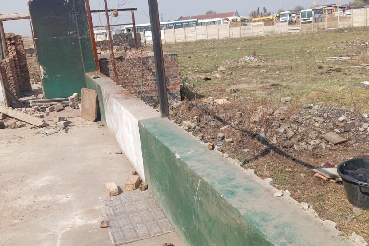 An outdoor industrial area featuring a concrete slab, low boundary wall, and metal support posts, showing signs of significant wear and unfinished construction.