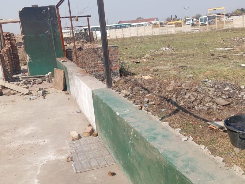 An outdoor industrial area featuring a concrete slab, low boundary wall, and metal support posts, showing signs of significant wear and unfinished construction.