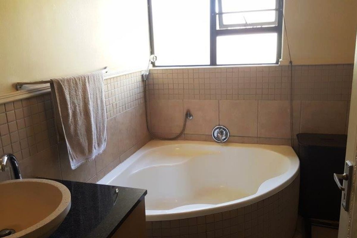 A functional bathroom featuring a corner bathtub, tiled splashback, and a vanity basin with a granite countertop.