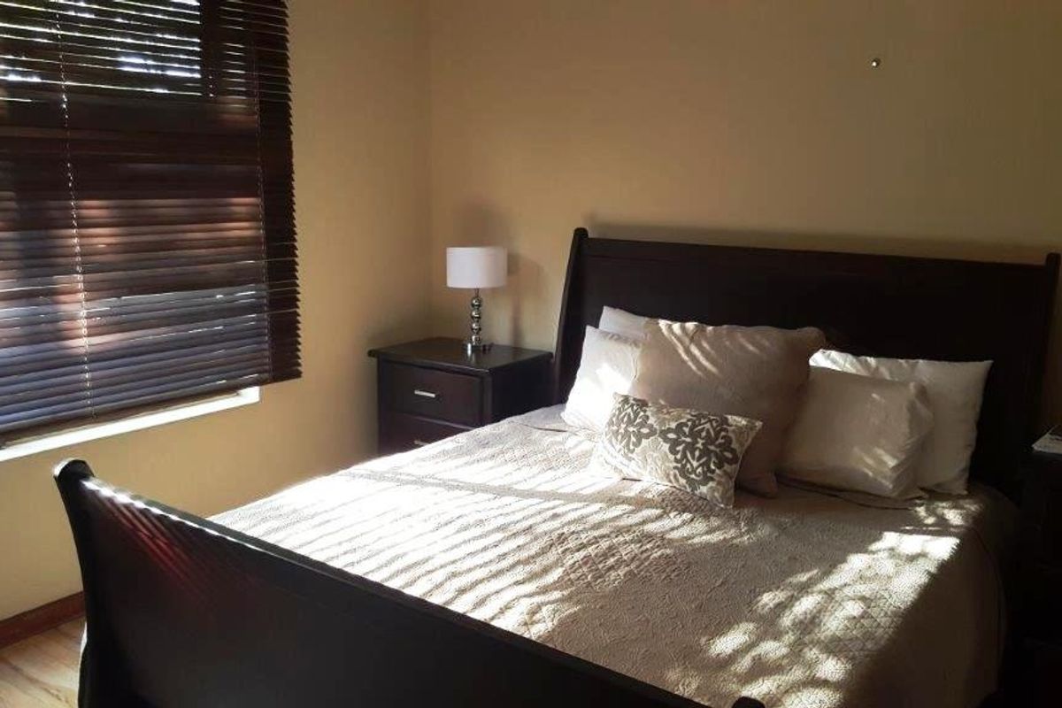 A comfortable bedroom featuring timber flooring and venetian blinds, providing a neutral and functional space.