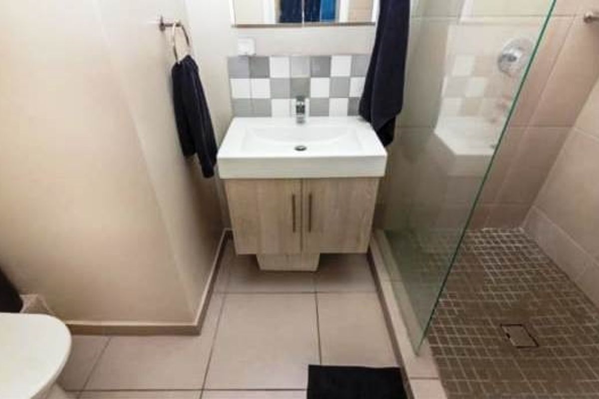 A functional bathroom featuring a modern vanity with basin, tiled splashback, and a walk-in shower with a glass screen.