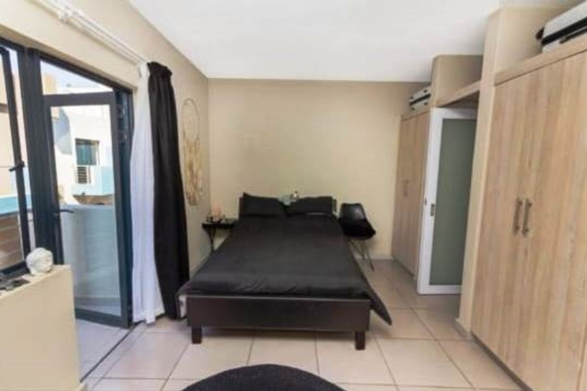 A bedroom featuring tiled flooring, built-in cupboards, and a sliding glass door providing access to an outdoor area.