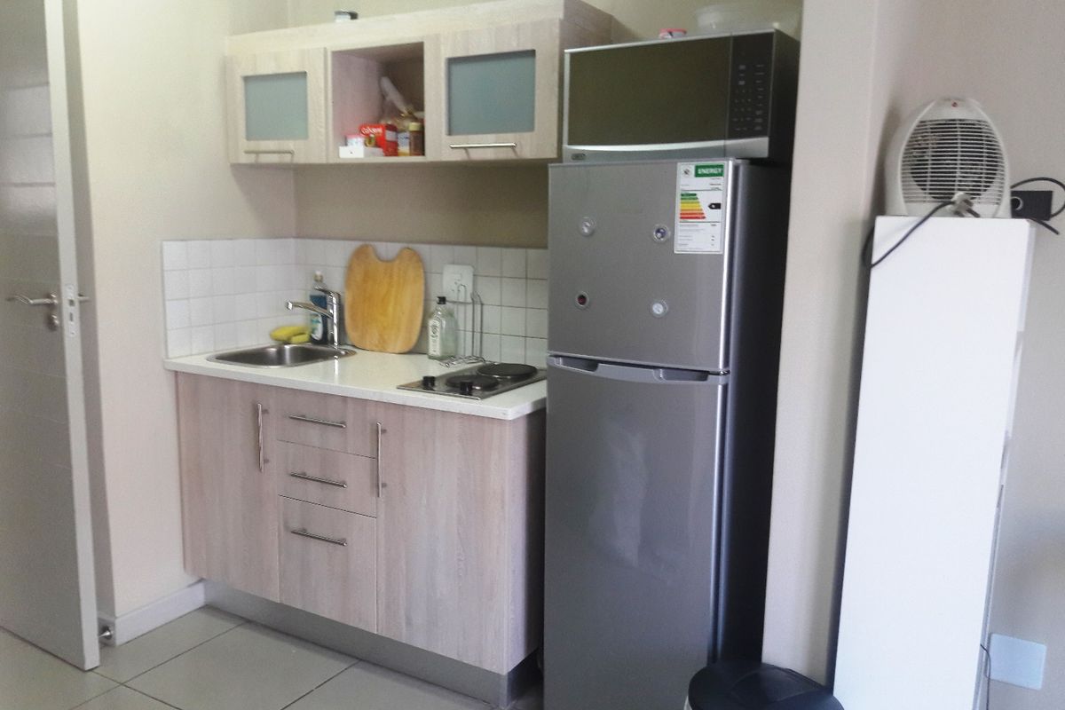 Compact kitchenette featuring light wood-look cabinetry, a stainless steel sink, tiled splashback, and a built-in electric hob.
