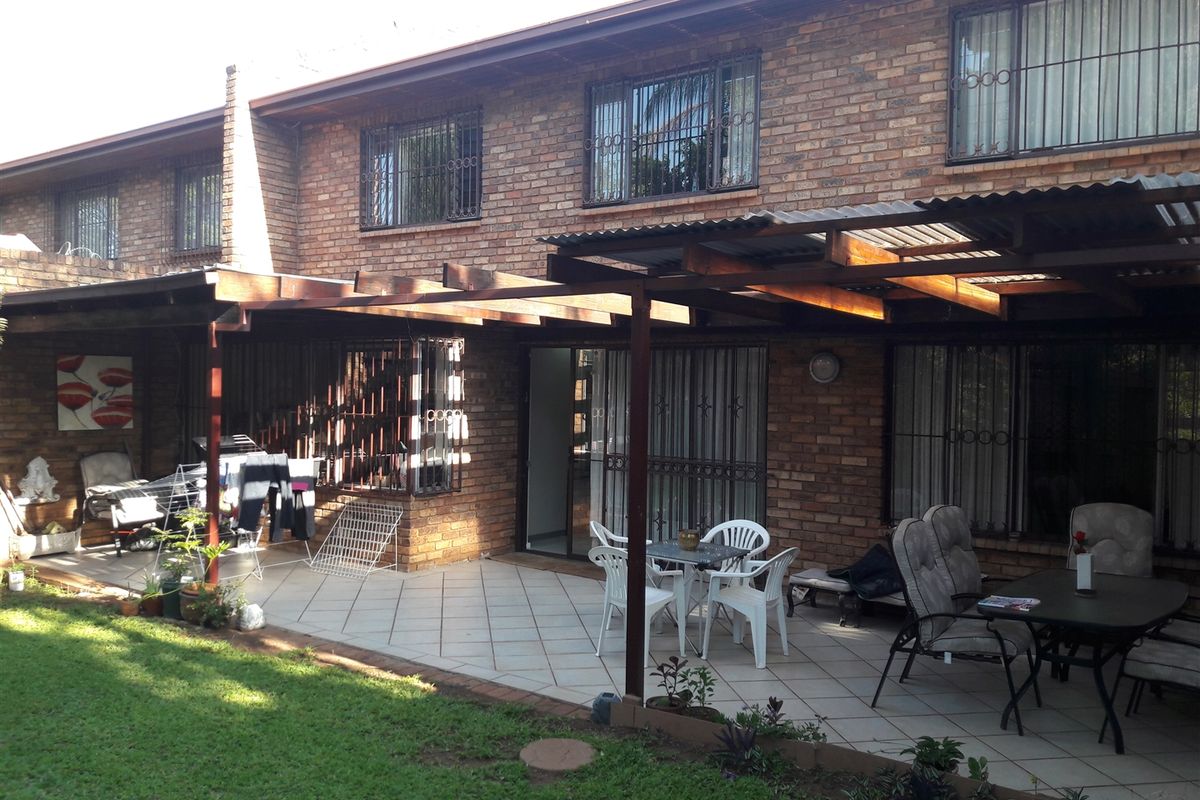 Rear view of a townhouse featuring a spacious tiled patio covered by a timber pergola, overlooking a private garden area.