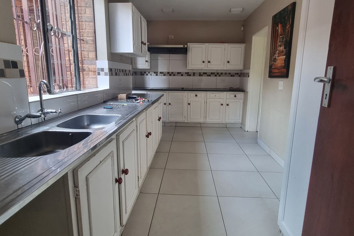 A functional kitchen featuring white built-in cabinetry, a double stainless steel sink, tiled backsplash, and ceramic floor tiles.