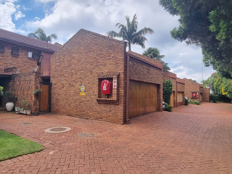 Front view of a facebrick townhouse complex featuring a paved driveway, double garage, and established garden surroundings.