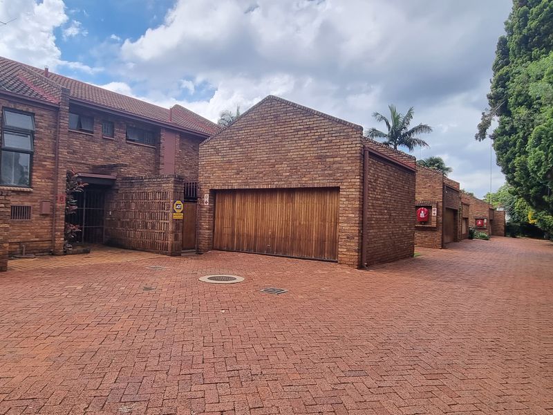 Front exterior view of a face brick townhouse complex featuring a paved driveway and integrated timber garage doors.