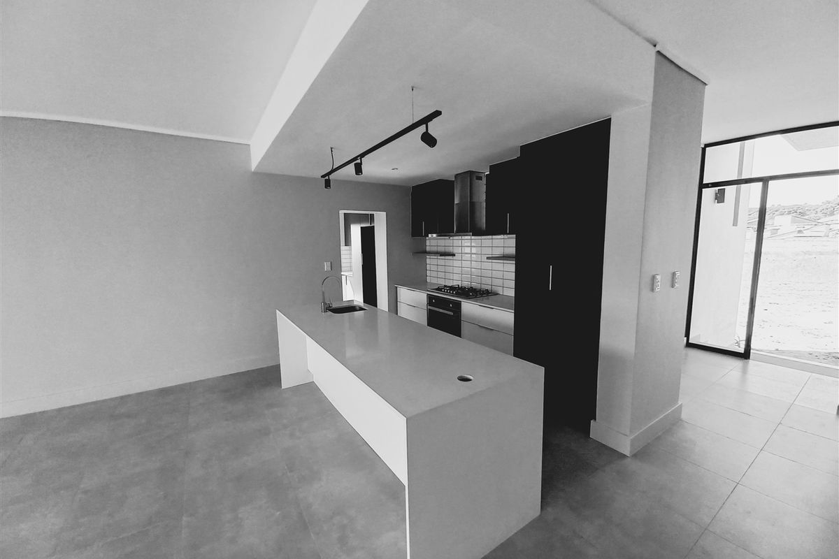 Modern open-plan kitchen featuring a central island, built-in oven, gas hob, extractor fan, and sleek cabinetry with a subway tile backsplash.