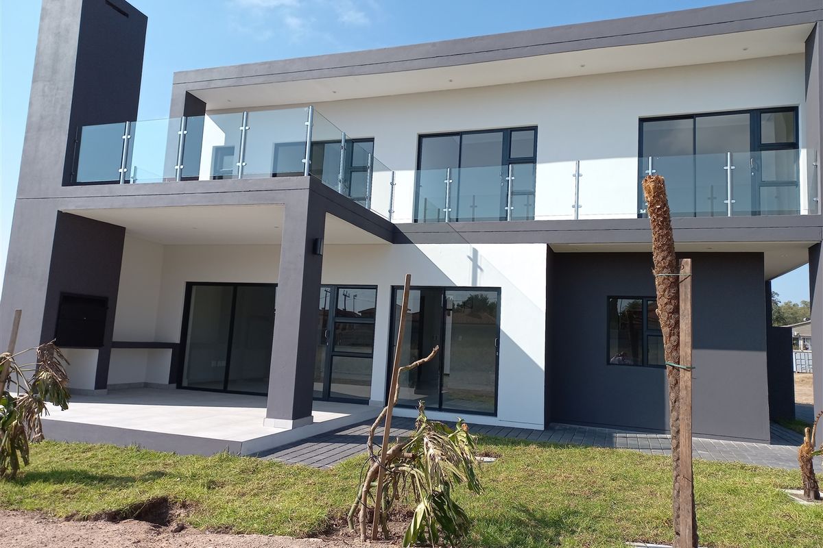 Modern double-story rear facade featuring a spacious covered patio with built-in braai, glass balustrades, and large sliding doors for seamless indoor-outdoor flow.