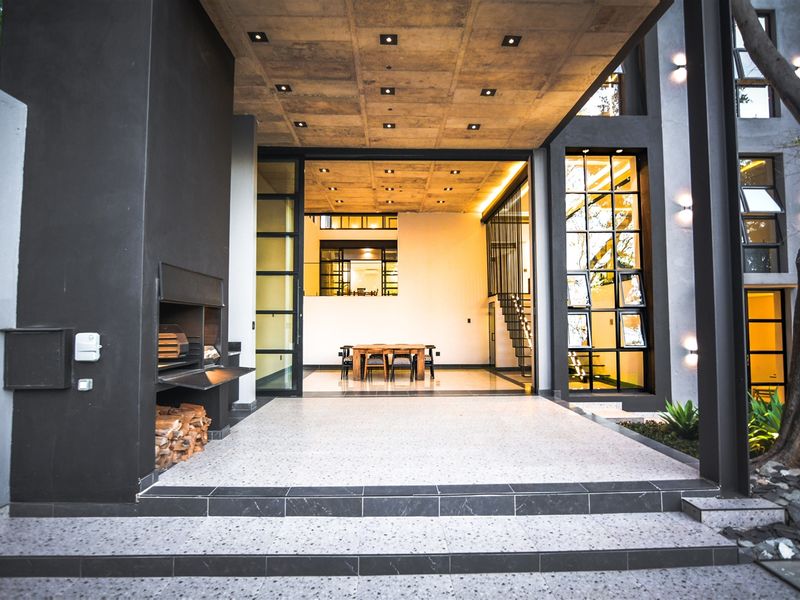 A modern covered patio featuring a built-in braai, terrazzo flooring, and an exposed concrete ceiling, seamlessly connecting to the interior living space.