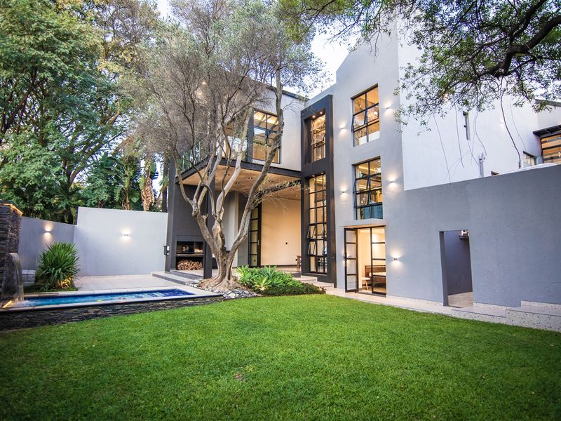 Modern double-story rear elevation featuring a landscaped garden, swimming pool with water feature, and a covered patio area with a built-in braai.