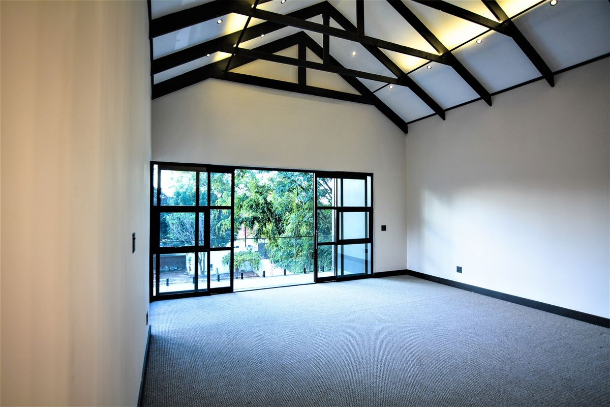 Spacious living area featuring a high vaulted ceiling with exposed timber trusses, recessed lighting, and large sliding glass doors opening to an outdoor view.
