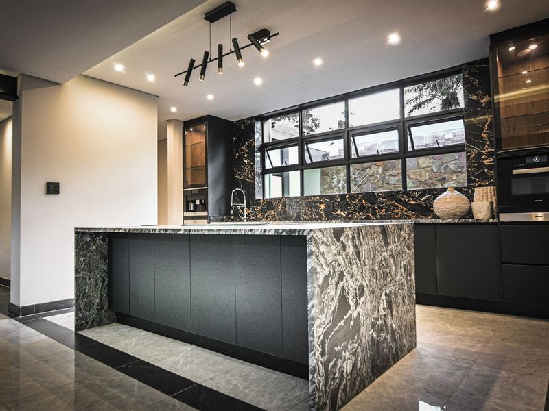 Modern luxury kitchen featuring a large stone-topped island, premium black cabinetry, built-in appliances, and elegant recessed lighting with high-end finishes throughout.