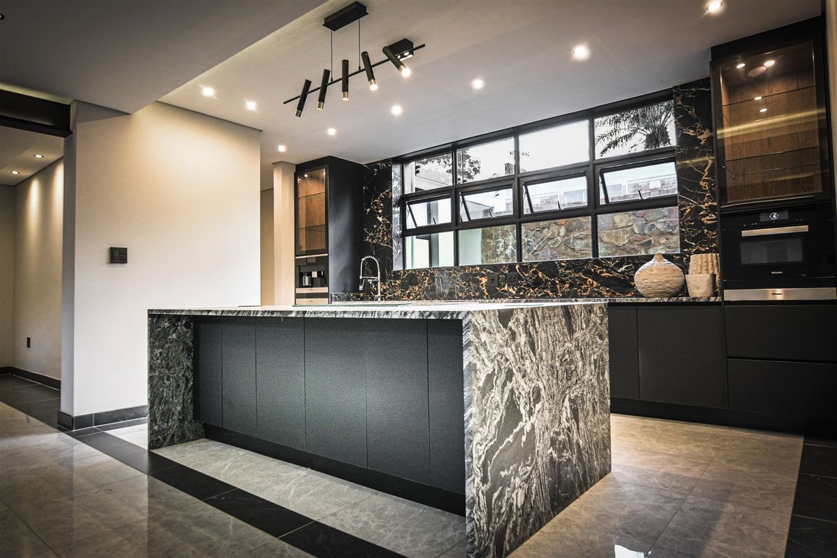 Modern luxury kitchen featuring a large stone-topped island, premium black cabinetry, built-in appliances, and elegant recessed lighting with high-end finishes throughout.