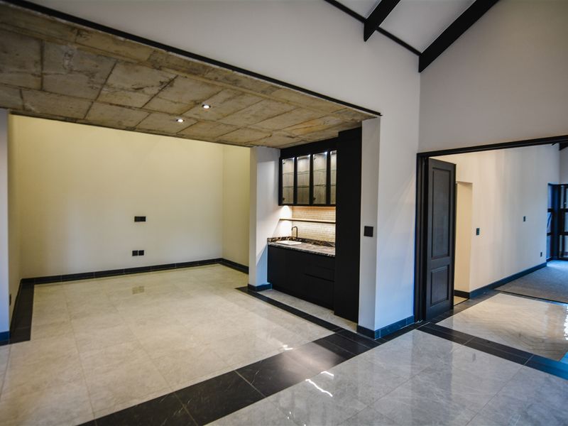 Spacious open-plan living area featuring a modern kitchenette with built-in cabinetry, sleek tiled flooring, and a striking exposed concrete ceiling.