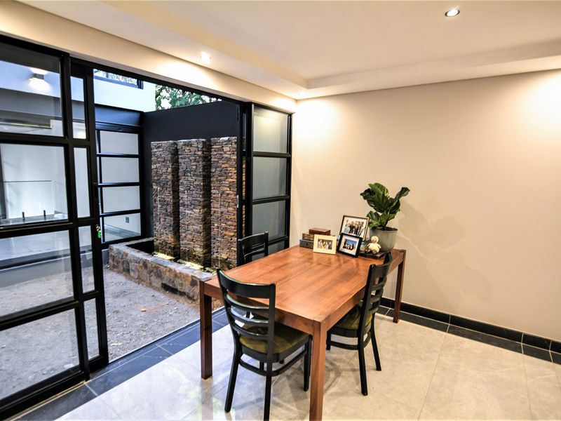 Dining area featuring modern tiled flooring, recessed lighting, and large black metal-framed glass sliding doors opening to an outdoor stone water feature.