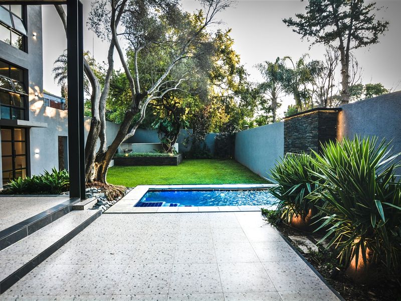 A beautifully landscaped rear garden featuring a modern swimming pool, stone feature wall, and spacious tiled patio area perfect for outdoor entertaining.