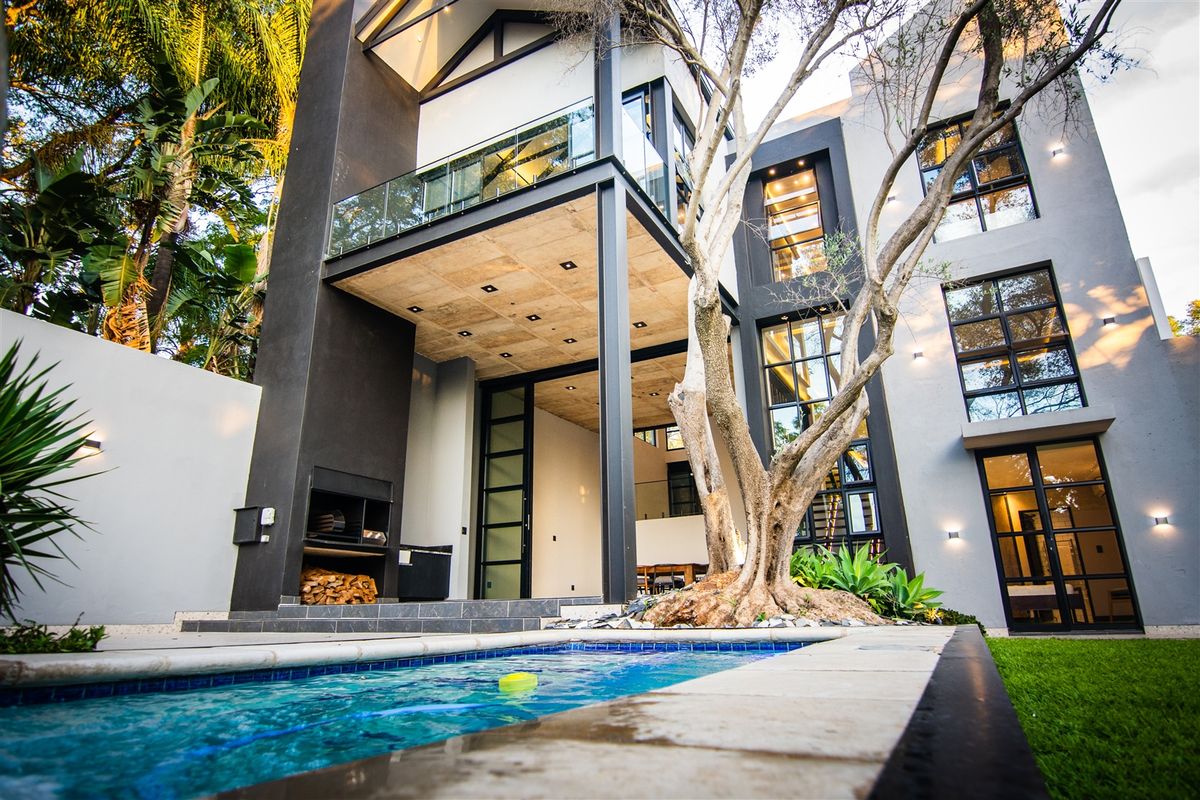 Modern multi-story rear elevation featuring a swimming pool, built-in outdoor fireplace, and a covered patio with exposed concrete ceiling and glass balcony.