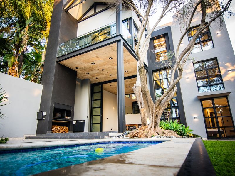 Modern multi-story rear elevation featuring a swimming pool, built-in outdoor fireplace, and a covered patio with exposed concrete ceiling and glass balcony.