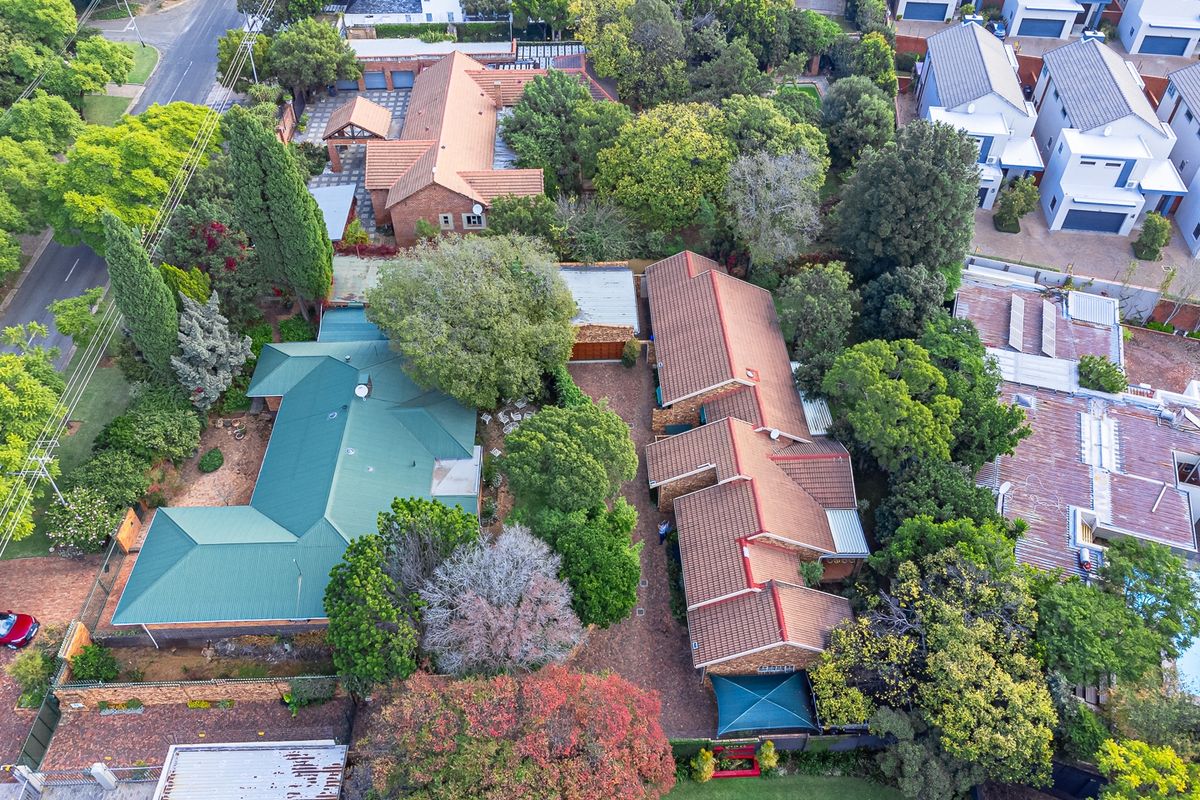 Aerial view of the property showcasing the main dwelling, secondary structures, mature garden, and paved driveway layout within the residential estate.