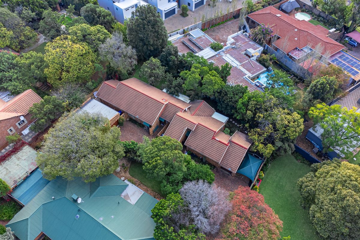 An aerial view of the property showcasing the main dwelling with a tiled roof, surrounding mature trees, landscaped garden, and paved driveway area.