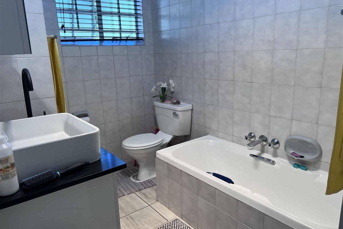 A functional bathroom featuring a built-in bathtub, wall-mounted basin, and toilet, finished with neutral wall and floor tiling.