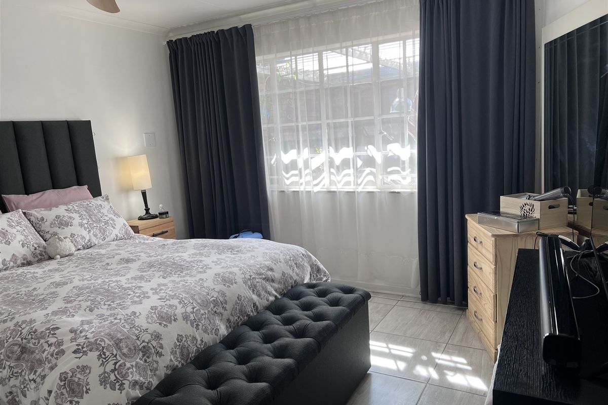 A well-maintained bedroom featuring tiled flooring, a ceiling fan, and large windows with dark curtains, providing a comfortable and functional living space.