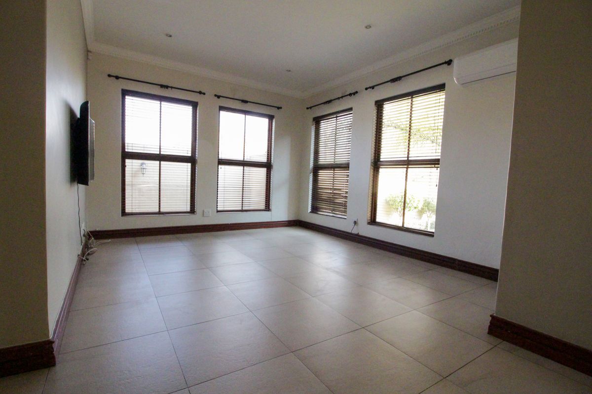 A bright, empty living room featuring large windows with blinds, tiled flooring, and a wall-mounted air conditioning unit.