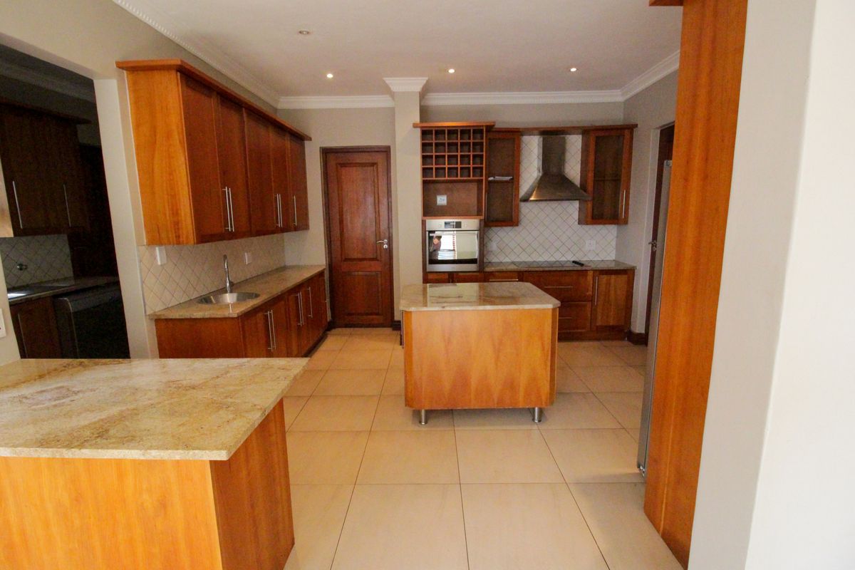 Spacious kitchen featuring warm wooden cabinetry, granite countertops, a central island, and built-in appliances, offering a functional and classic layout.