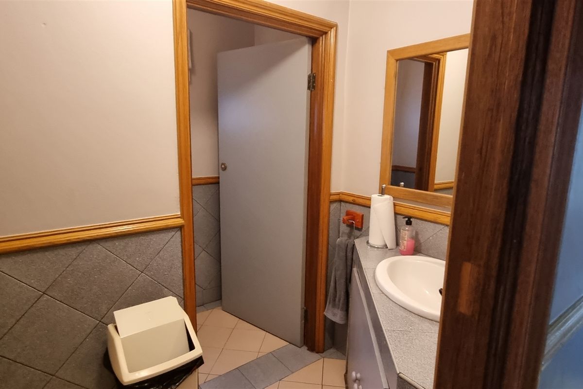 A functional bathroom featuring a vanity basin, wall mirror, and tiled wainscoting with classic timber trim detailing.