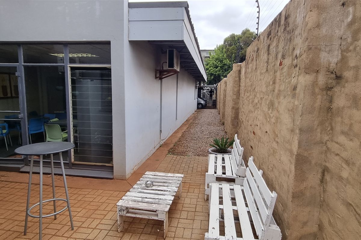 Rear exterior area featuring a paved patio, gravel walkway, and perimeter wall with electric fencing, providing access to the office building.