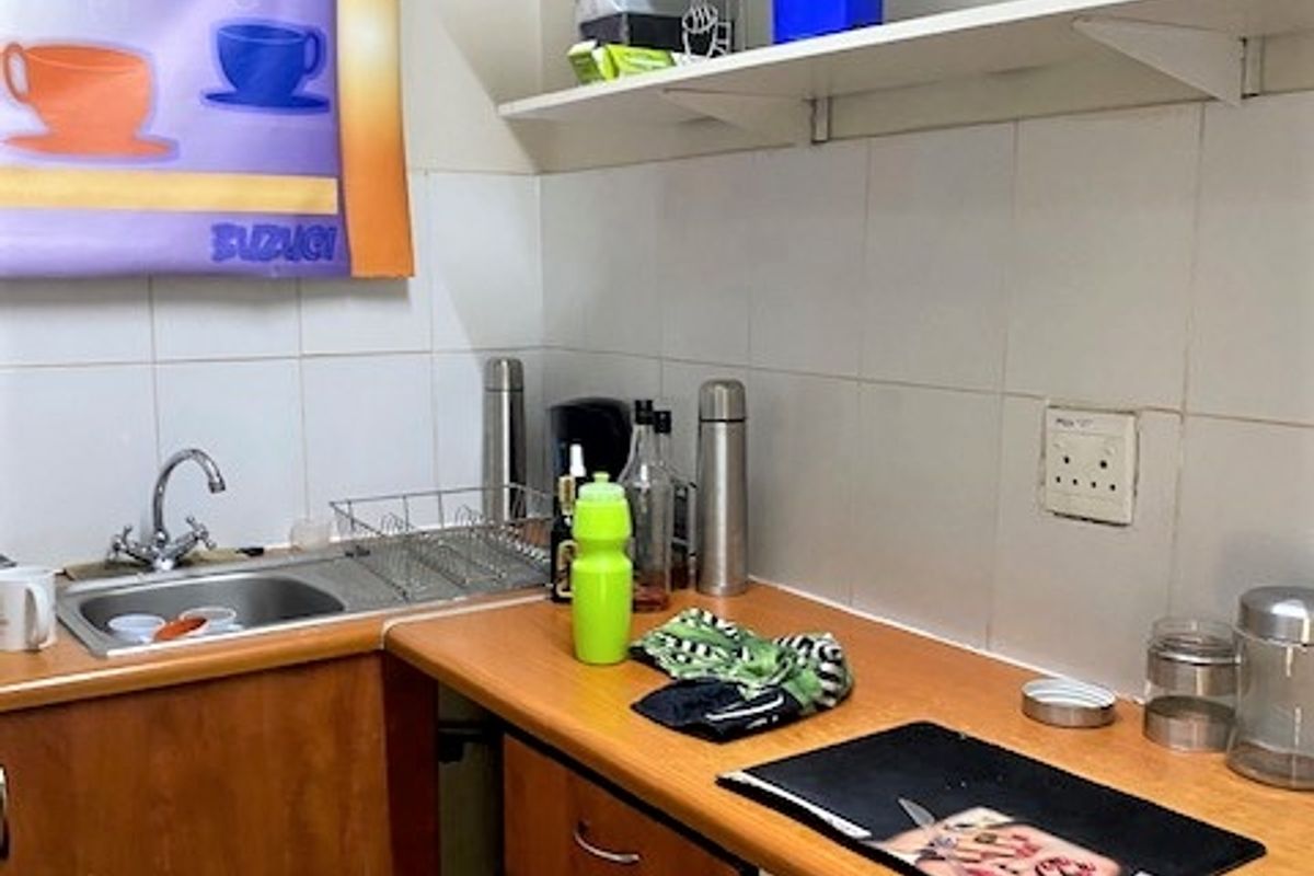 A compact kitchenette featuring wooden cabinetry, a stainless steel sink, tiled splashback, and open shelving for storage.