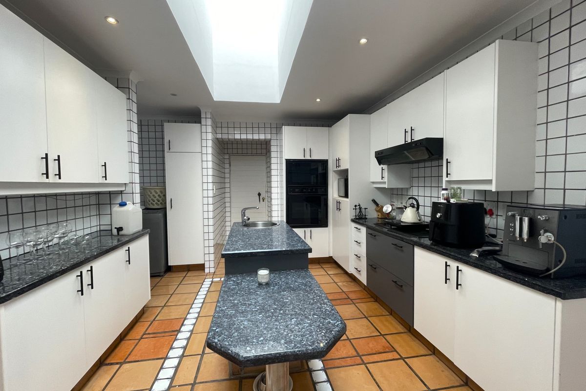 A spacious kitchen featuring a central island, built-in oven, extractor fan, and ample cabinetry, illuminated by a large overhead skylight.