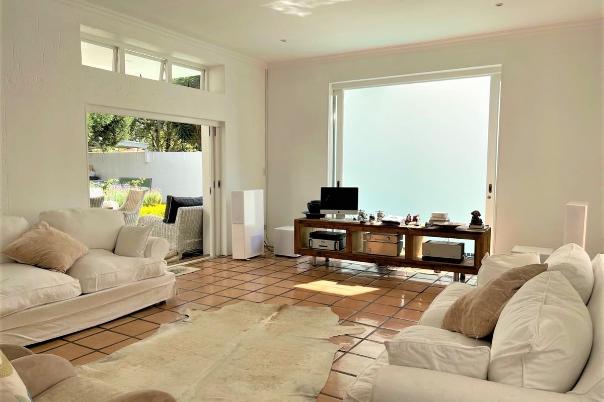 Spacious living room featuring terracotta floor tiles, high ceilings with clerestory windows, and large sliding glass doors providing seamless access to the outdoor patio area.