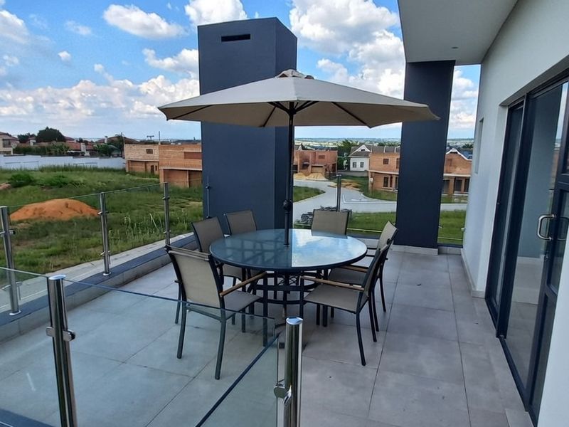 A modern covered balcony featuring tiled flooring, a glass balustrade, and sliding door access, offering an open view of the surrounding neighborhood.