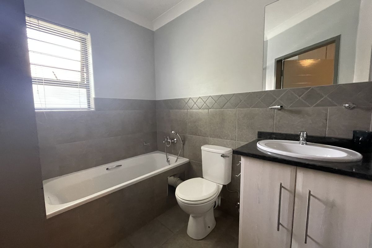 A clean, functional bathroom featuring a built-in bathtub, a vanity with a basin, and neutral wall tiling.