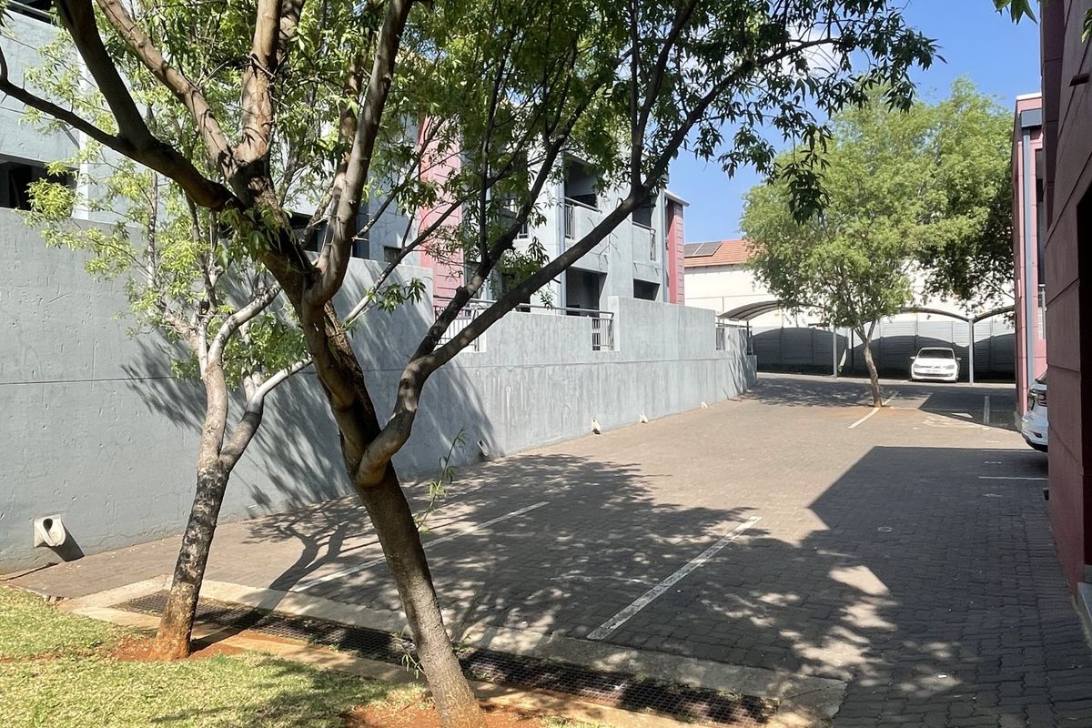 A paved outdoor parking area featuring covered bays, retaining walls, and established trees within an apartment complex setting.