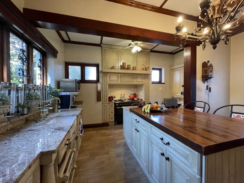 A charming farmhouse-style kitchen featuring granite countertops, a large timber-topped island, exposed ceiling beams, and a classic gas range with a built-in extractor hood.