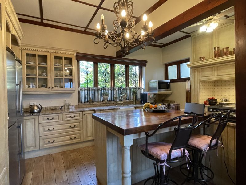 A rustic-style kitchen featuring a large wooden island, stone countertops, custom cabinetry, exposed ceiling beams, and a decorative wrought iron chandelier.