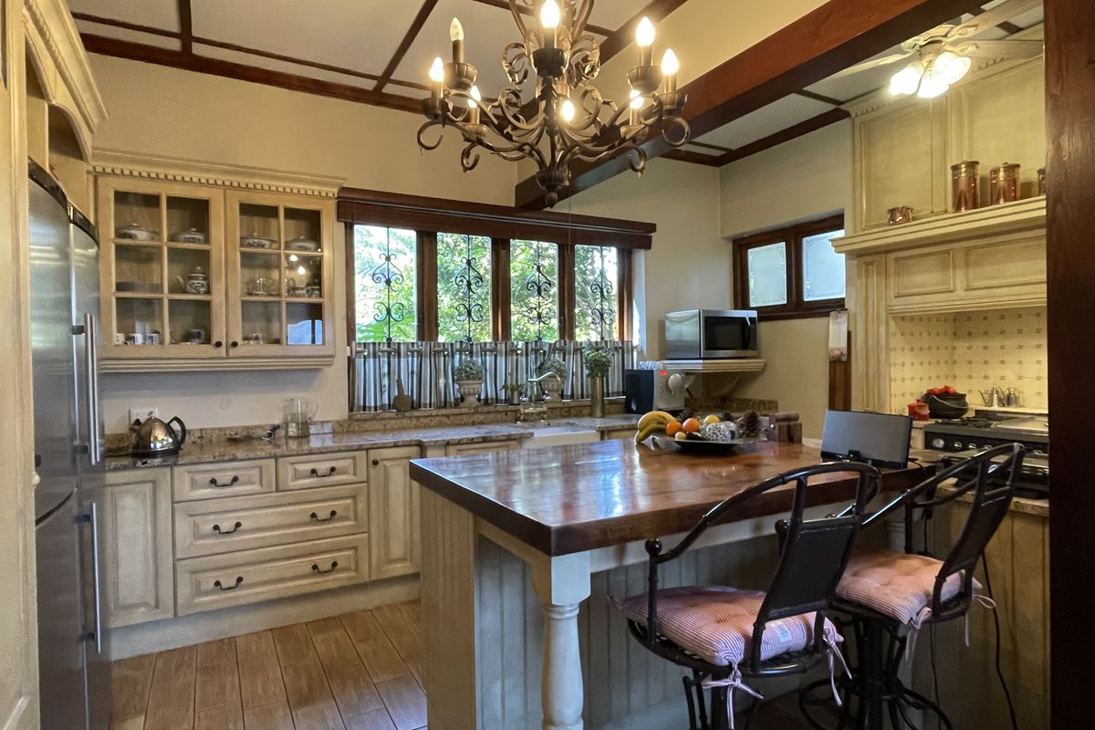 A rustic-style kitchen featuring a large wooden island, stone countertops, custom cabinetry, exposed ceiling beams, and a decorative wrought iron chandelier.