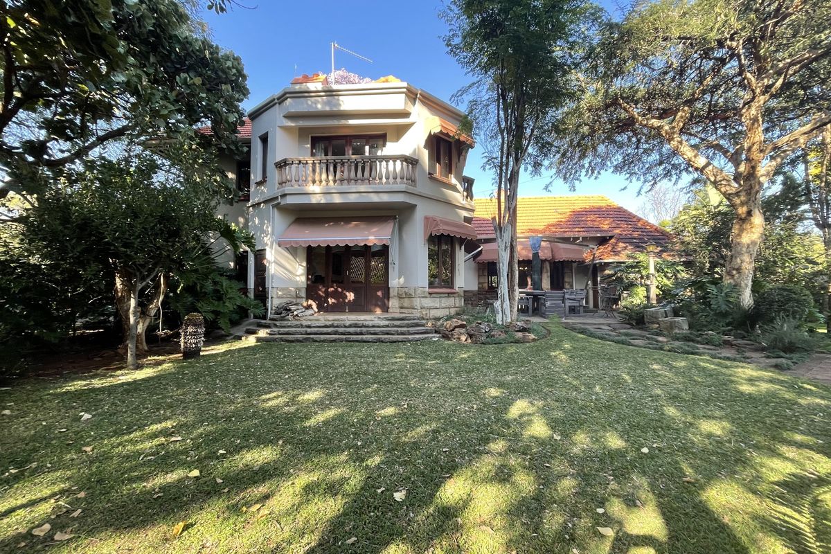 Rear view of a multi-story house featuring a balcony, stone detailing, terracotta roof tiles, and a spacious garden area.