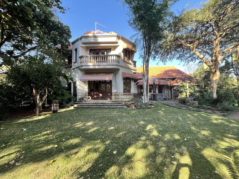 Rear view of a multi-story house featuring a balcony, stone detailing, terracotta roof tiles, and a spacious garden area.
