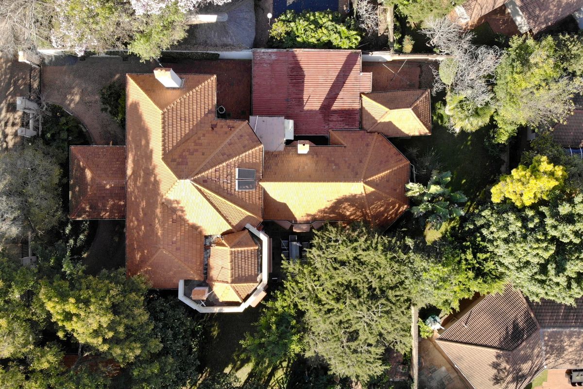 Aerial view of the property showcasing the extensive terracotta tile roof structure, chimney, and surrounding landscaped garden area.