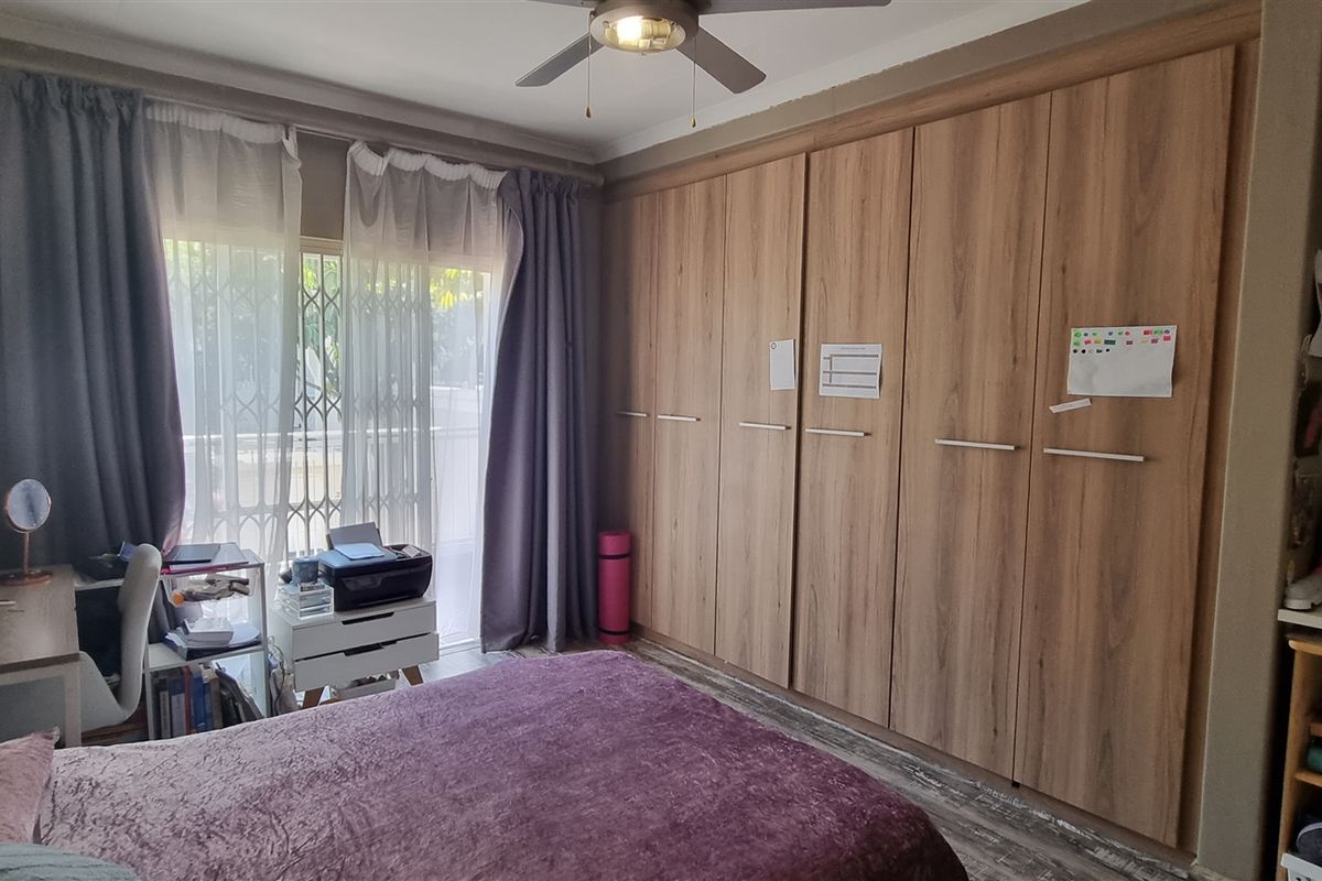 A bedroom featuring extensive built-in wooden cupboards, a ceiling fan, air conditioning, and a sliding door leading to an outdoor area with a security gate.
