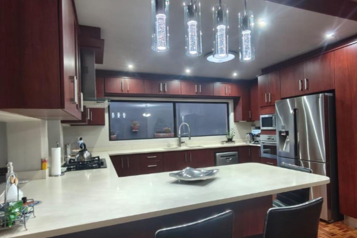 Modern kitchen featuring dark wood cabinetry, stone countertops, a central island, and integrated stainless steel appliances with contemporary pendant lighting.