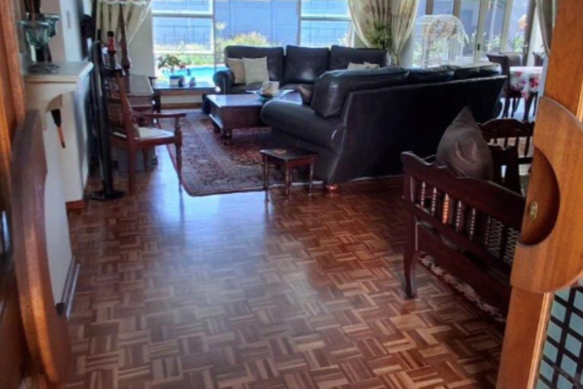 Spacious living area featuring classic parquet timber flooring and large windows providing natural light and views of the outdoor pool area.