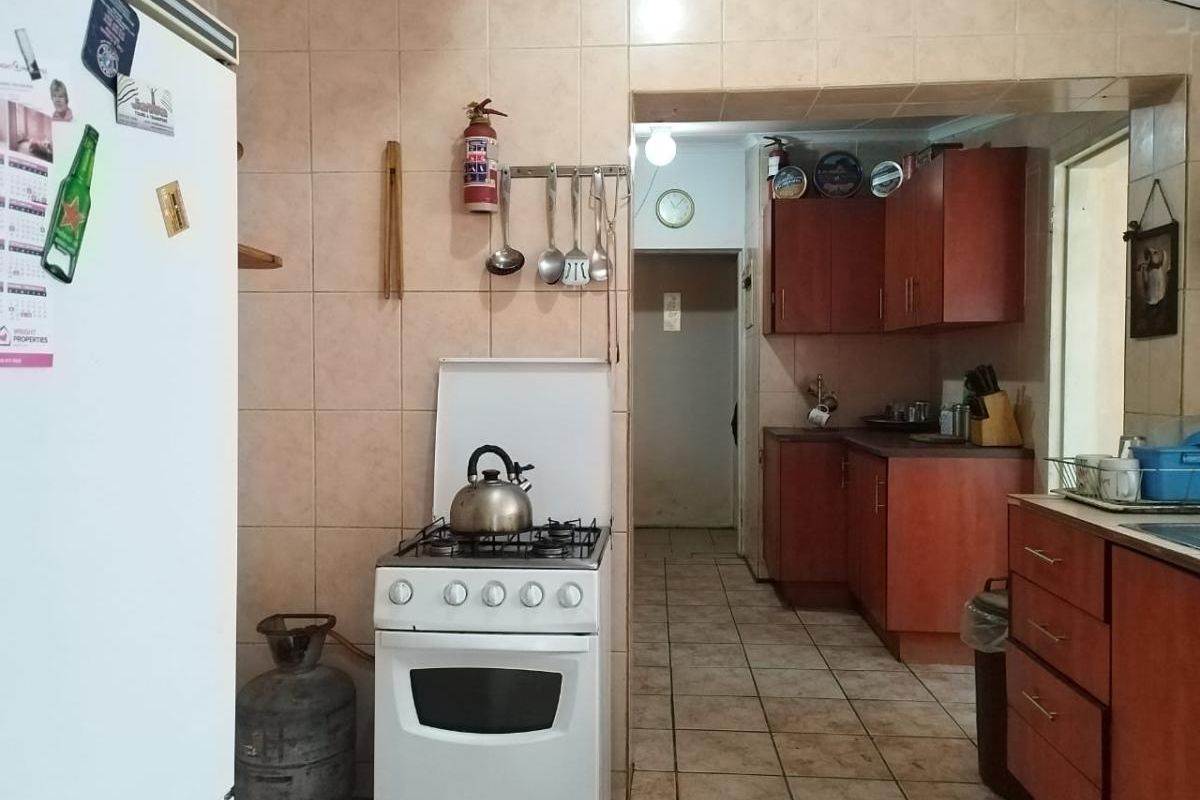 A functional kitchen featuring tiled walls, wooden cabinetry, and a gas stove, with an adjoining scullery or prep area.