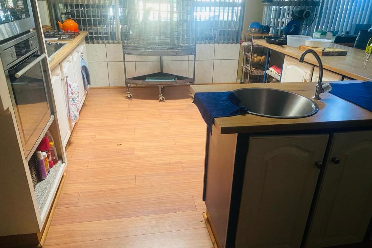 A functional kitchen featuring wood-look laminate flooring, built-in oven, hob, and a central island with a stainless steel sink.